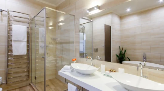 Plombier à genoux découpant un tuyau en acier galvanisé corrodé dans le mur ouvert d'une salle de bain de duplex montréalais en rénovation.
